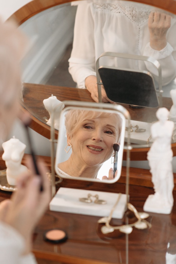 A woman smiling at her reflection while doing her makeup